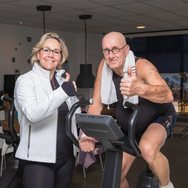 Coach en lid geven een duim omhoog bij een Milon-fiets