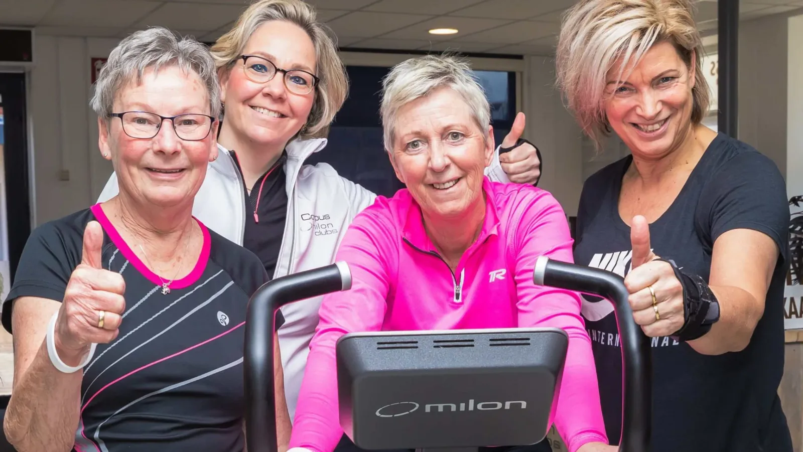 Vier leden geven een duim omhoog rond een Milon-fiets